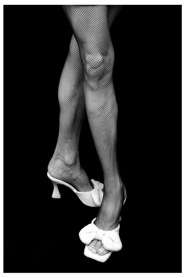 Black and white photograph of a pair of legs in fishnet tights and white kitten heels.