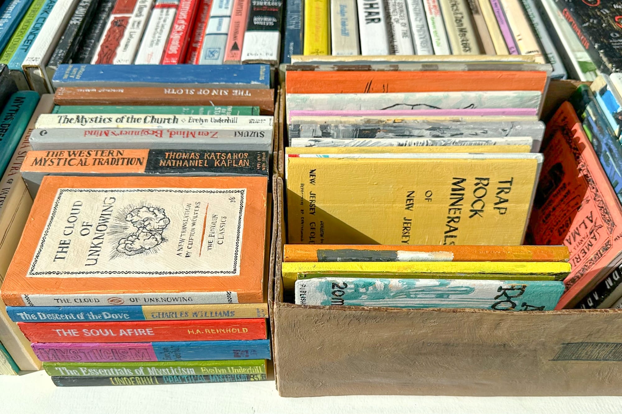 a collection of wooden and painted book sculptures by Conrad Bakker in boxes on a table