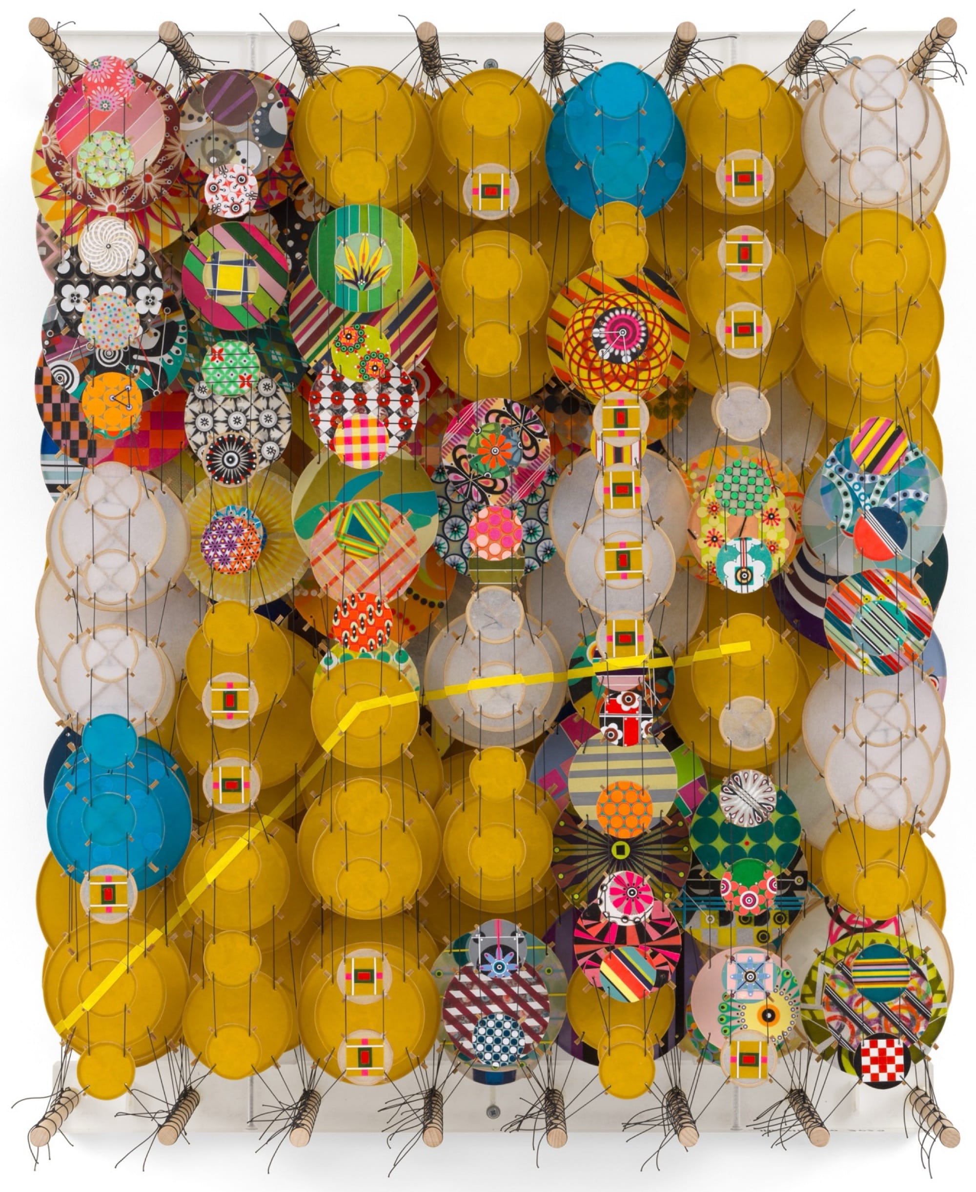 an abstract artwork by Jacob Hashimoto made from twine and numerous colorful, patterned paper discs installed in rows for a layered effect