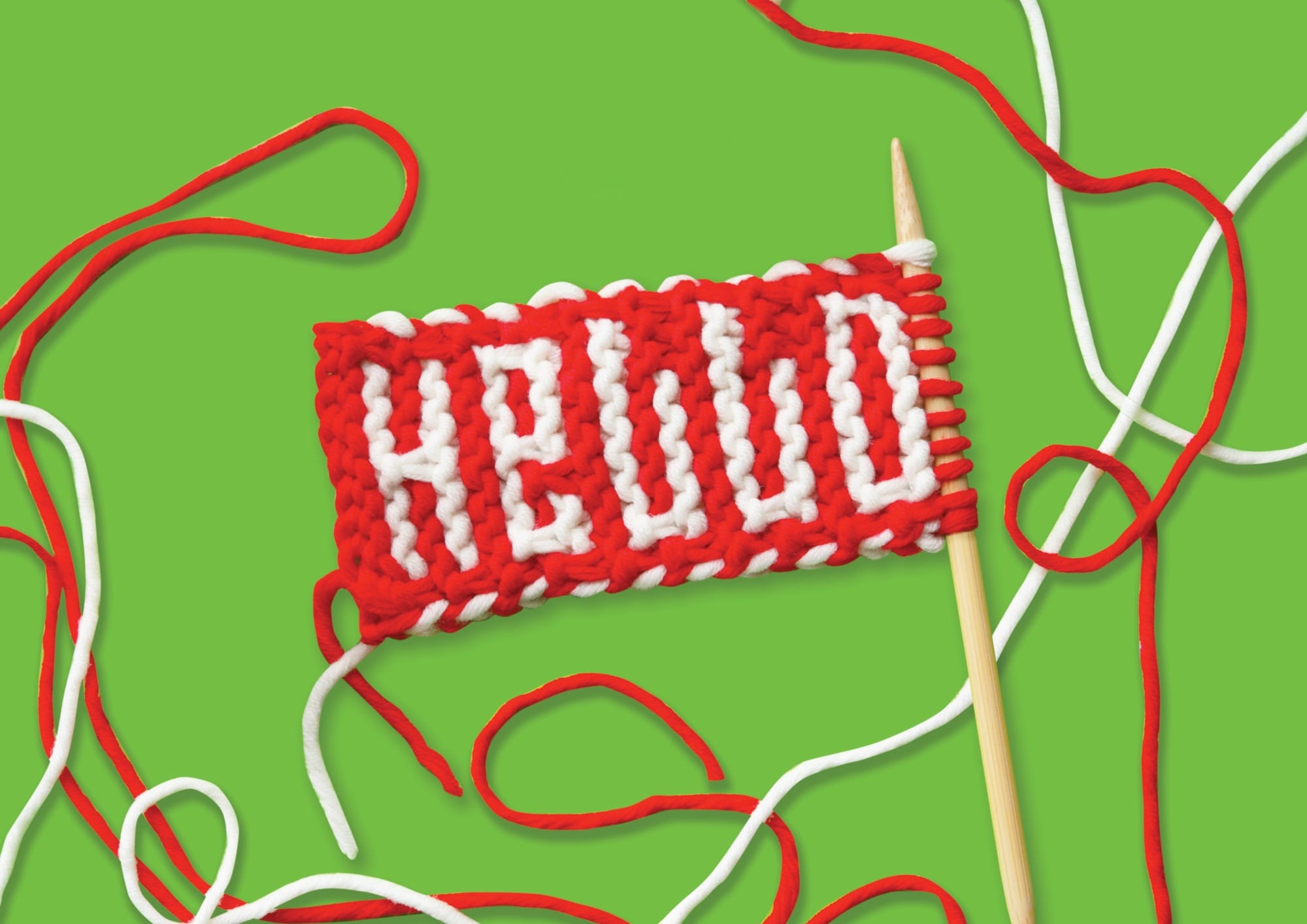 a small knitted fabric piece that reads "HELLO" in red and white yarn, with knitting needles and yarn around it