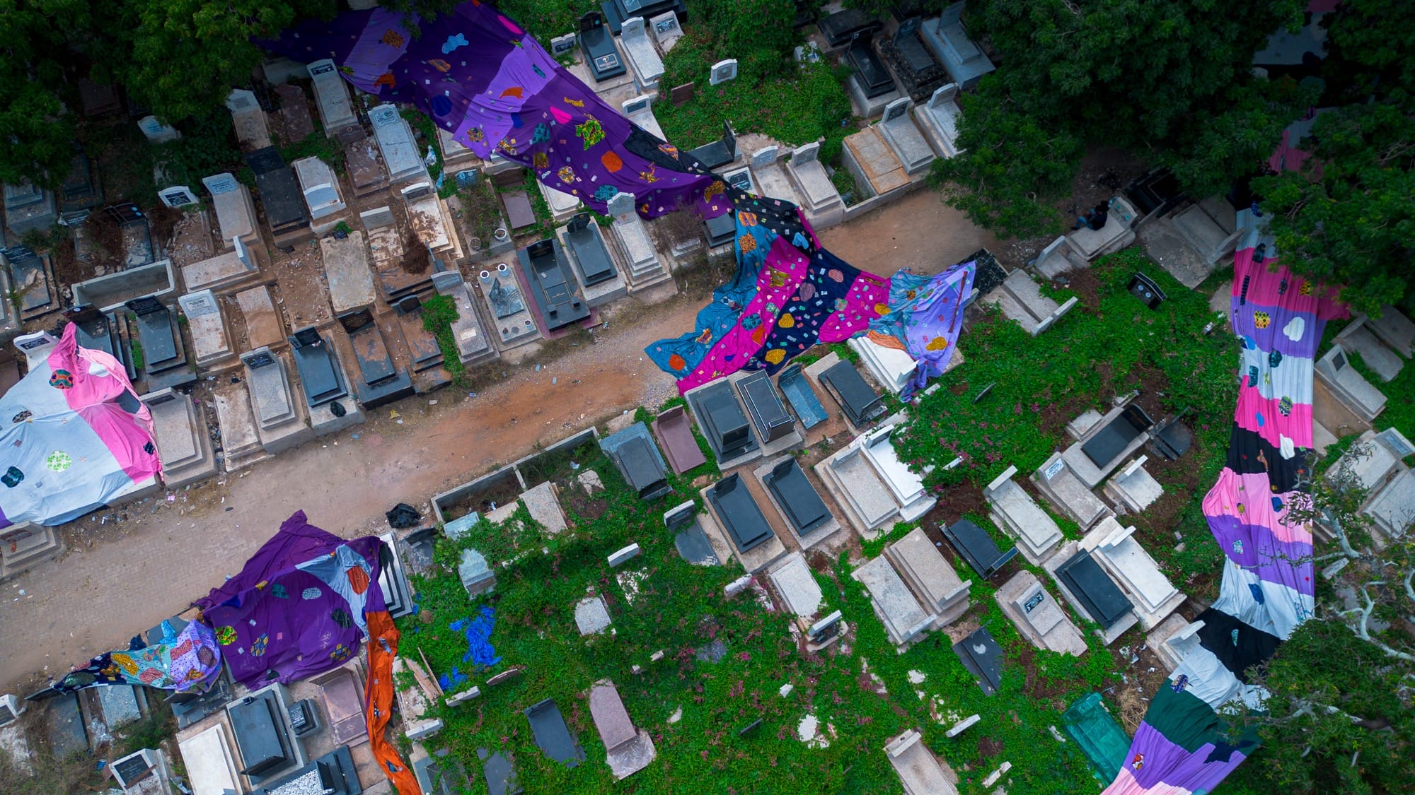 an aerial view of purple and pink fabric flying in the wind in a cemetary