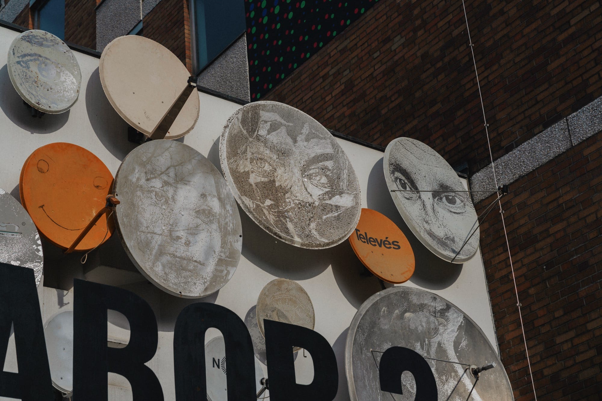 an installation by vhils of circular paintings with faces on a building