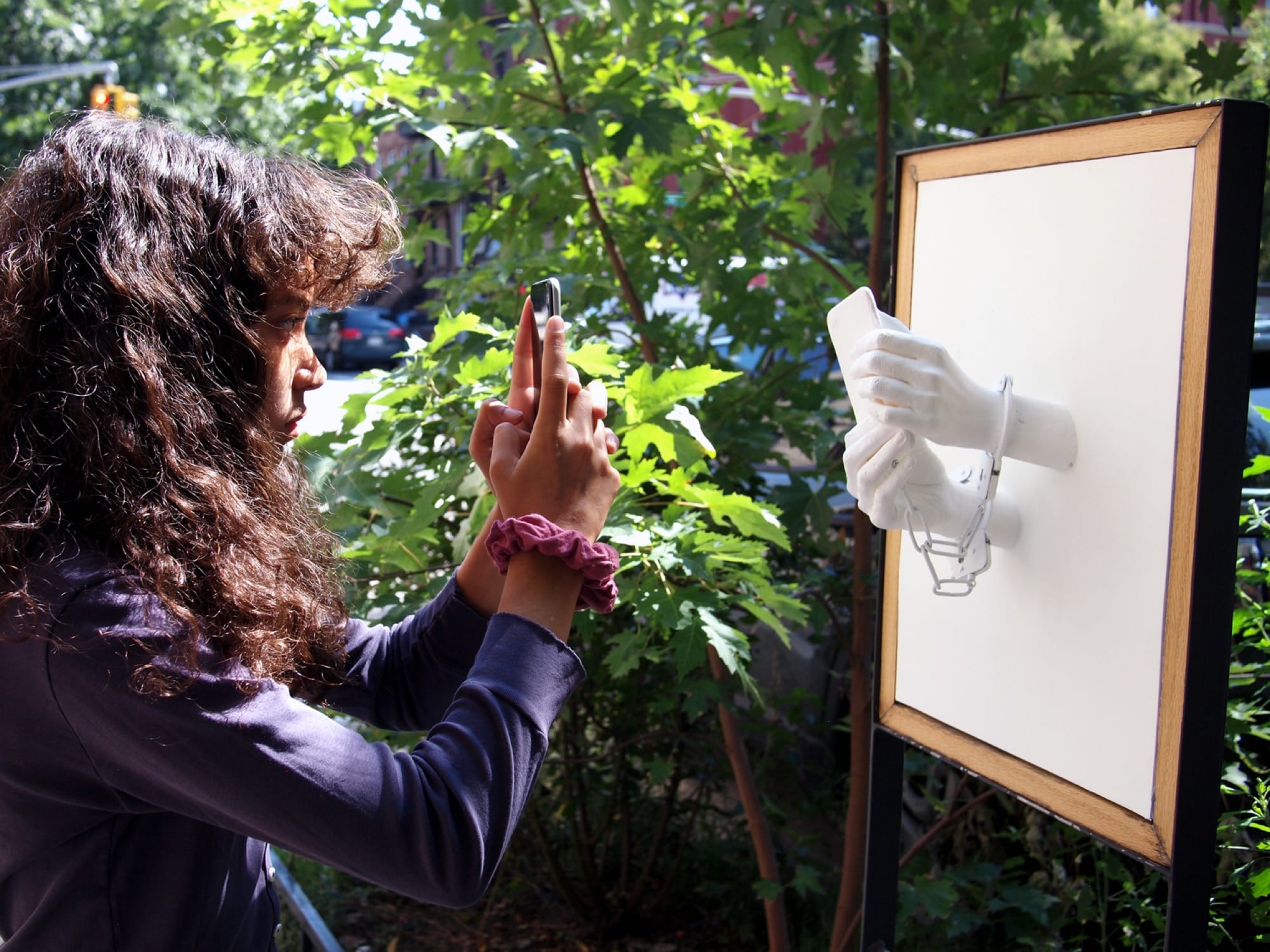 Leon Reid IV's sculpture of two hands holding a phone emerging from a white panel with handcuffs around the wrists