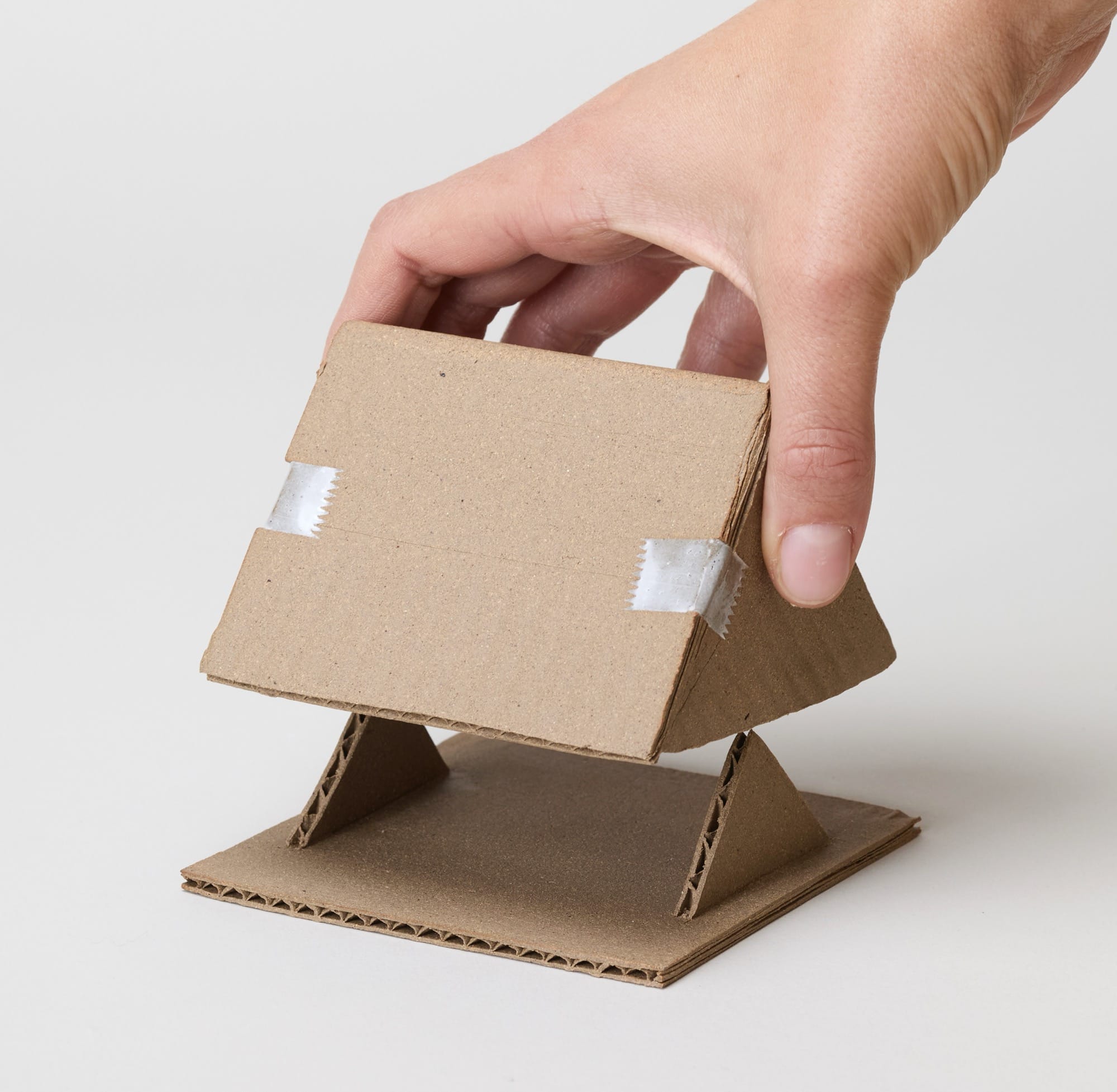 a hand reaches for a small ceramic sculpture by Jacques Monneraud that resembles cardboard with tape