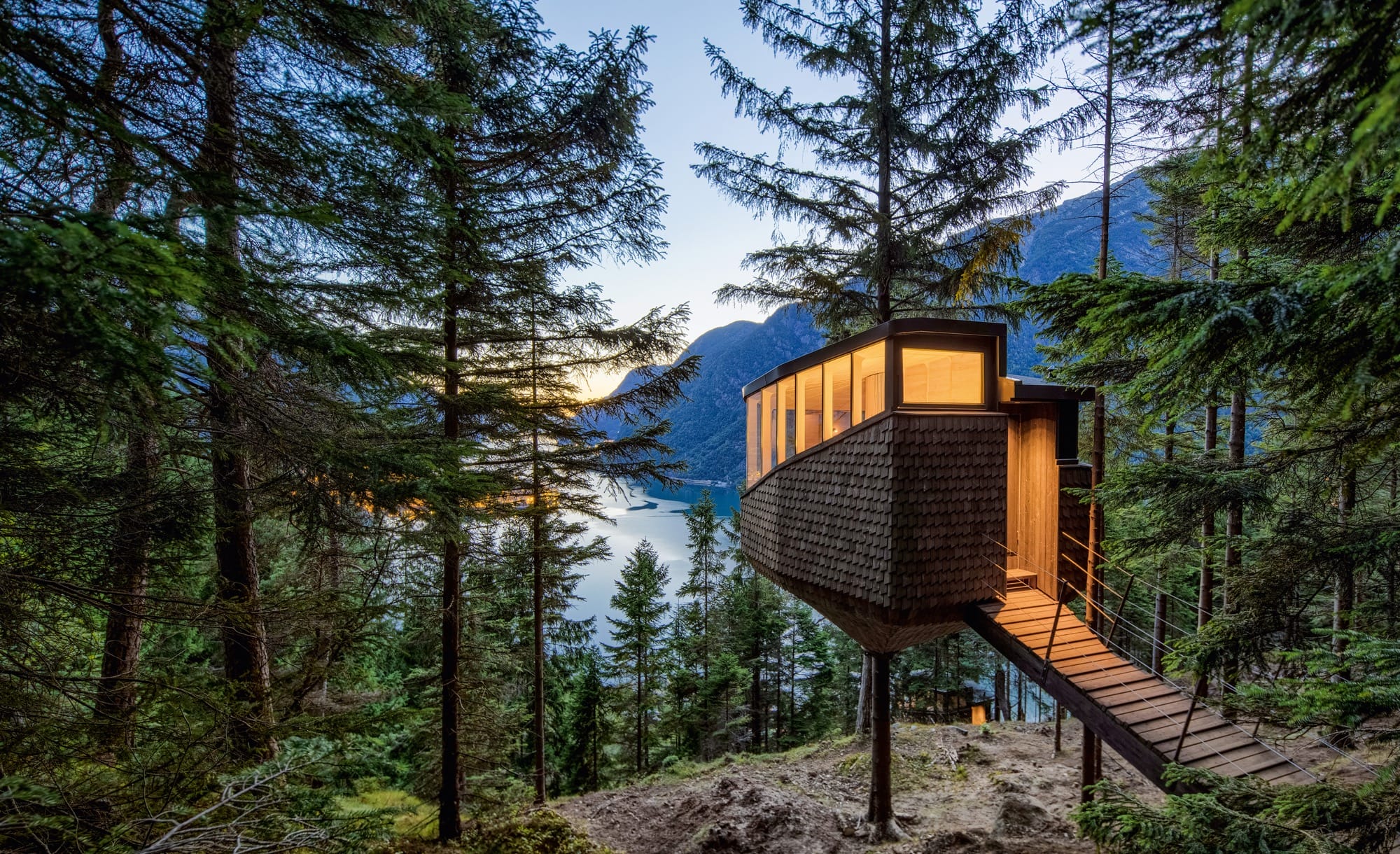 a modern treehouse in the forest overlooking a lake